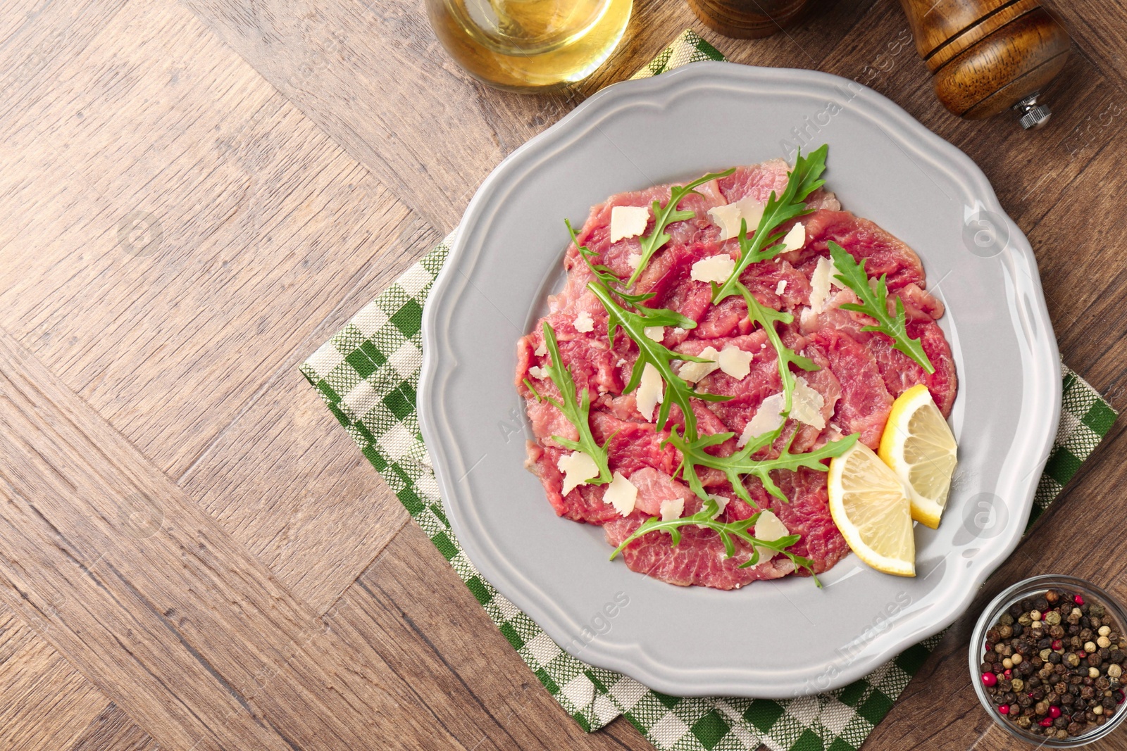 Photo of Fresh beef carpaccio with arugula, cheese and lemon on wooden table, flat lay. Space for text