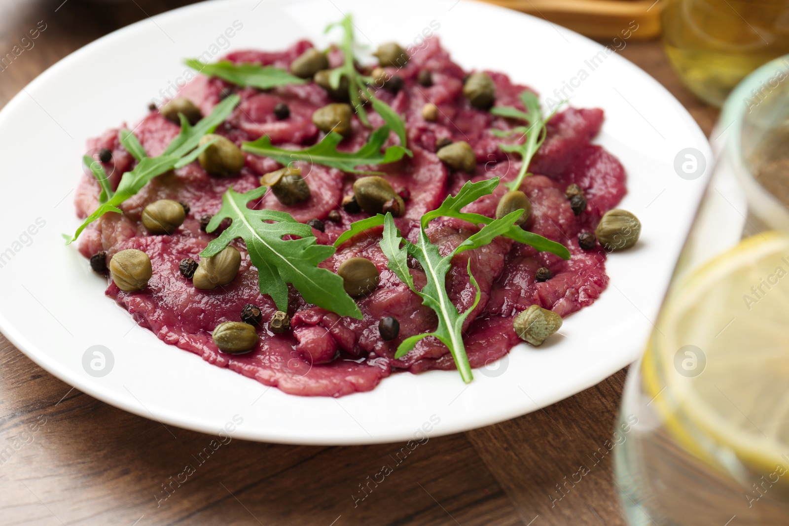 Photo of Fresh beef carpaccio with arugula and capers on wooden table, closeup