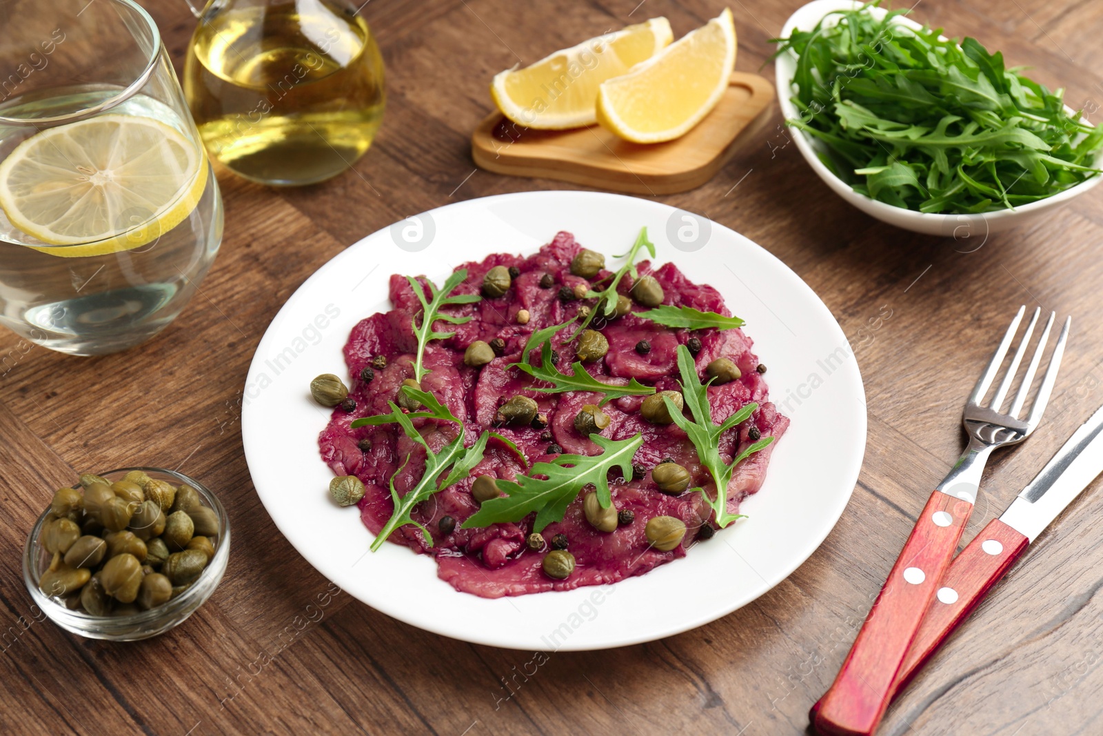 Photo of Fresh beef carpaccio with arugula and capers on wooden table