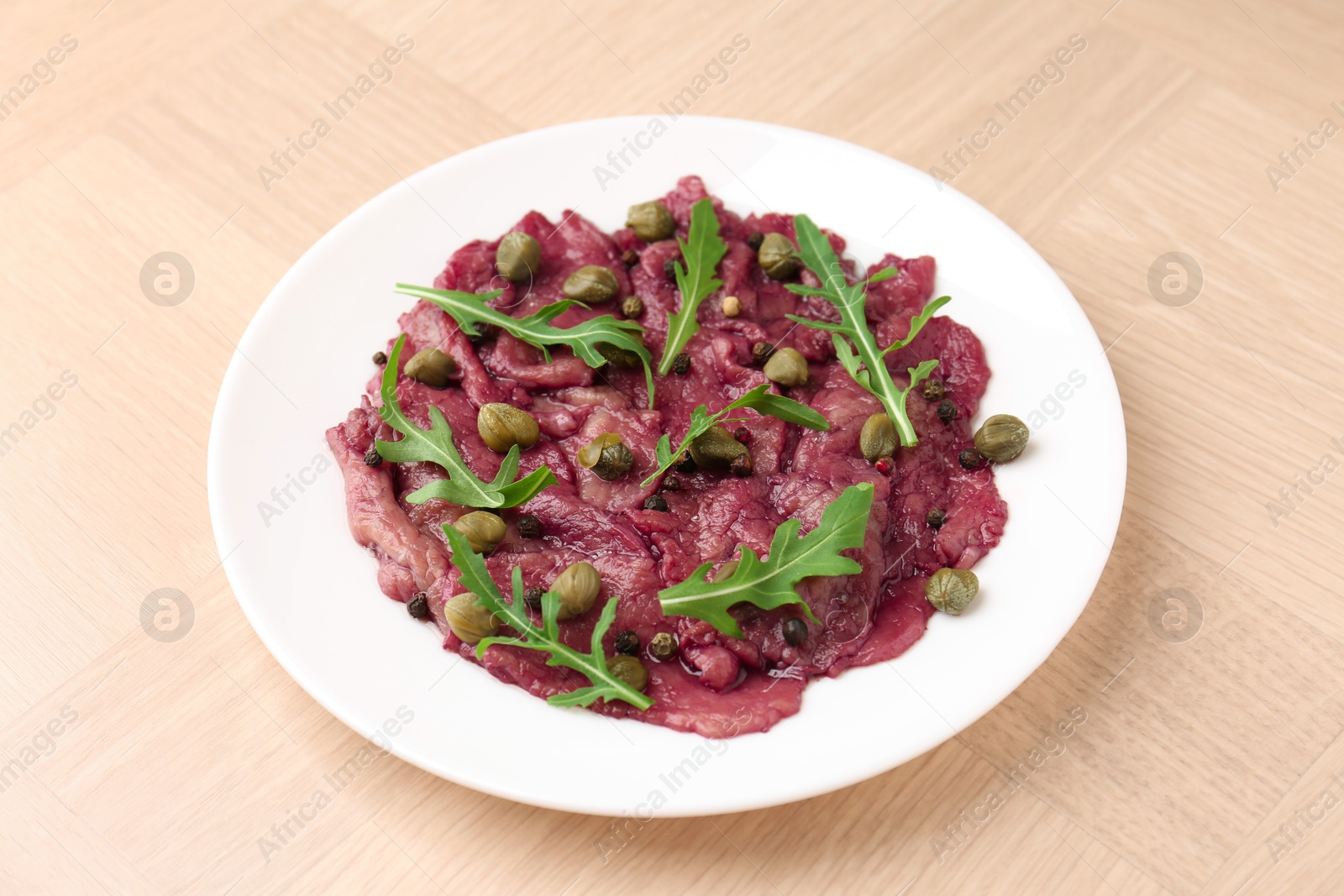 Photo of Fresh beef carpaccio with arugula and capers on wooden table, closeup