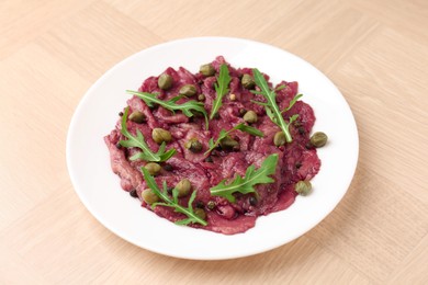 Photo of Fresh beef carpaccio with arugula and capers on wooden table, closeup