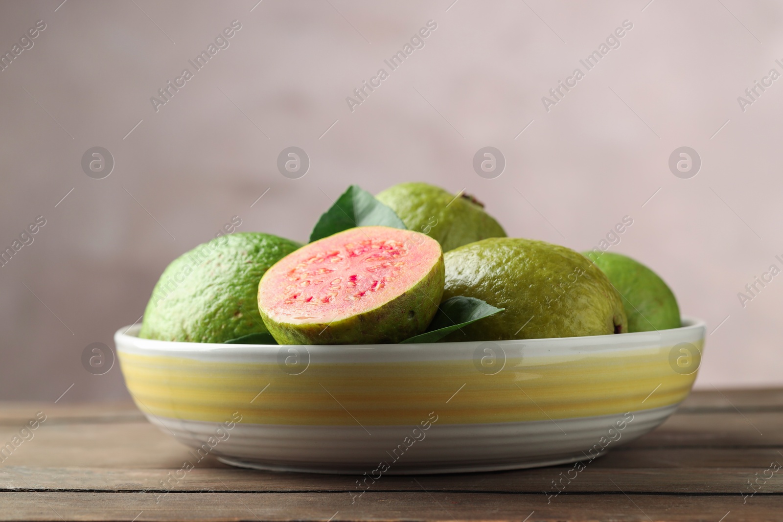 Photo of Fresh guava fruits in bowl on wooden table against blurred grey background, closeup