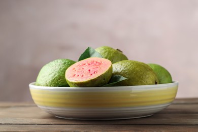 Fresh guava fruits in bowl on wooden table against blurred grey background, closeup