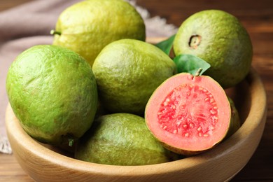 Photo of Fresh cut and whole guava fruits in bowl on table, closeup