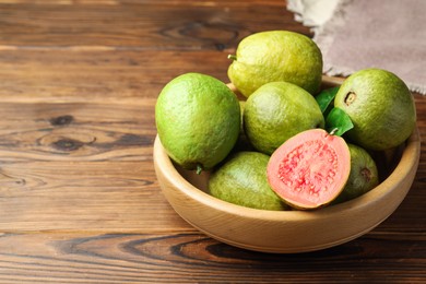 Fresh cut and whole guava fruits in bowl on wooden table, closeup. Space for text