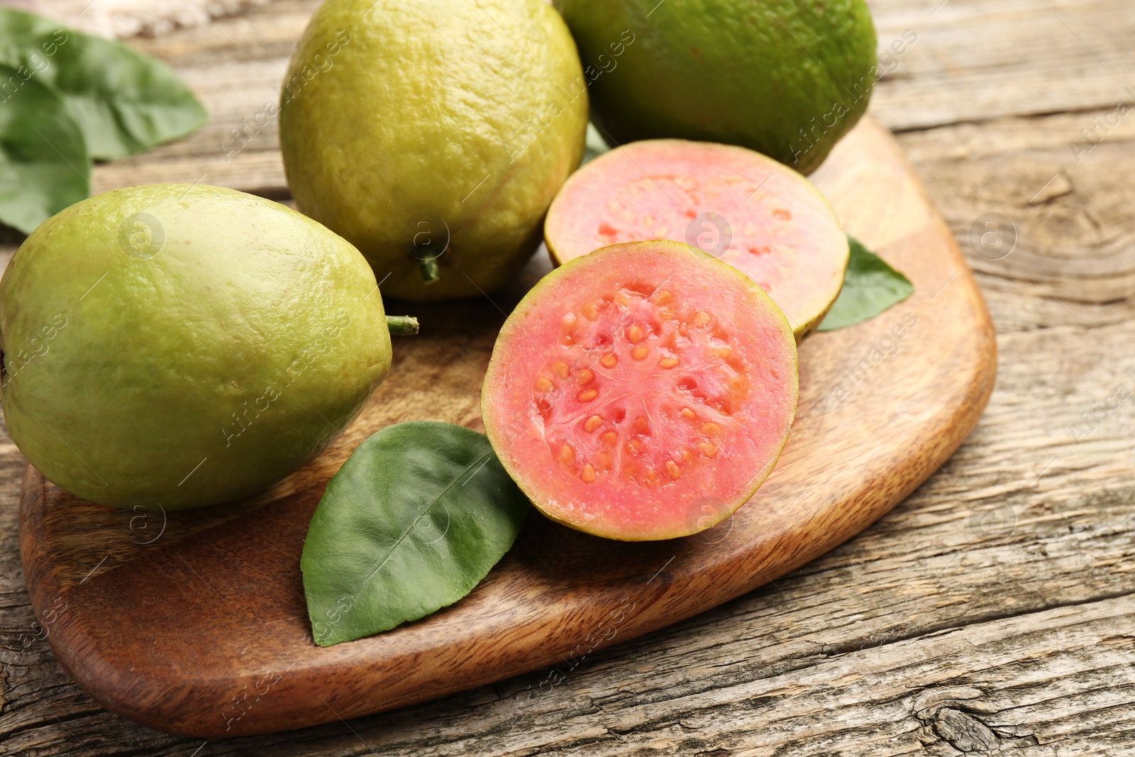 Photo of Fresh whole and cut guava fruits on wooden table, closeup