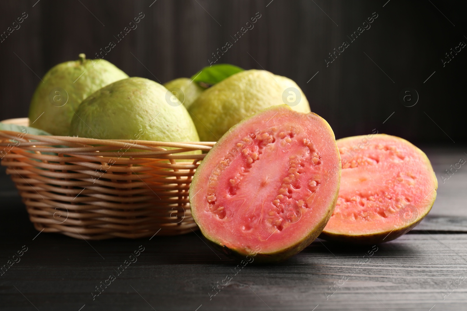 Photo of Fresh whole and cut guava fruits on black wooden table, closeup