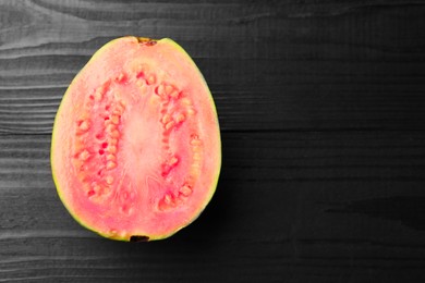 Photo of Half of fresh guava fruit on black wooden table, top view. Space for text