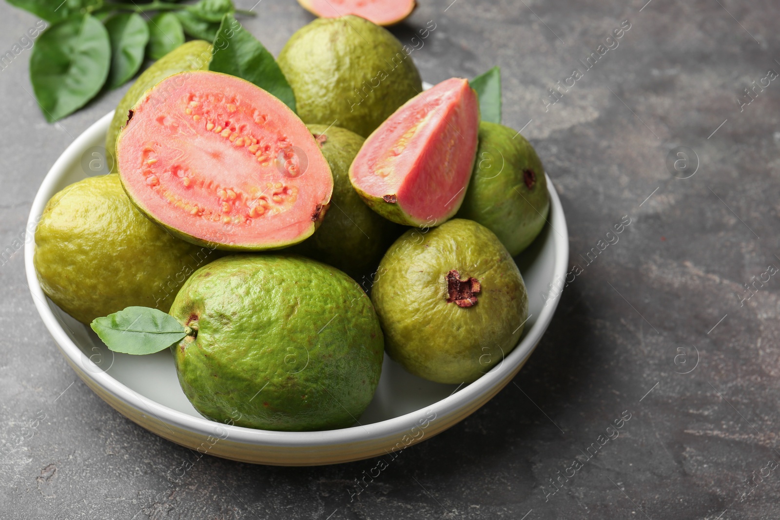 Photo of Fresh whole and cut guava fruits in bowl on grey textured table, closeup