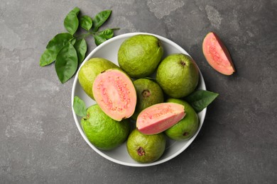 Photo of Fresh whole and cut guava fruits in bowl on grey textured table, top view