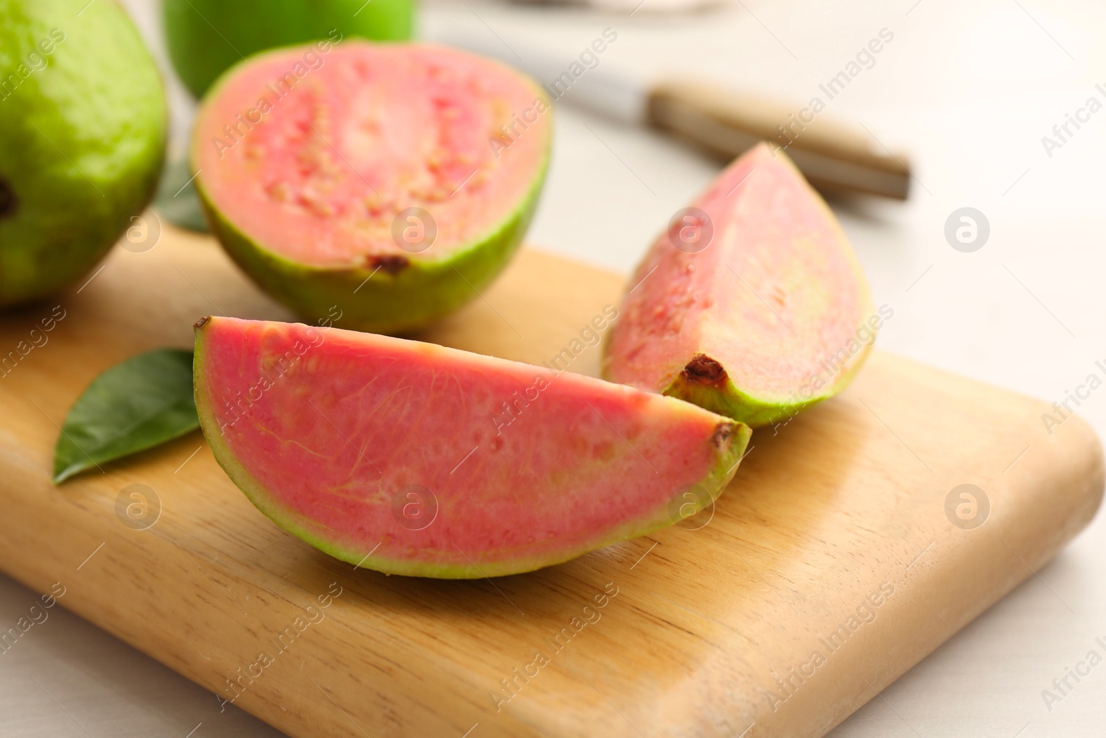 Photo of Fresh guava fruits and wooden board on white table, closeup