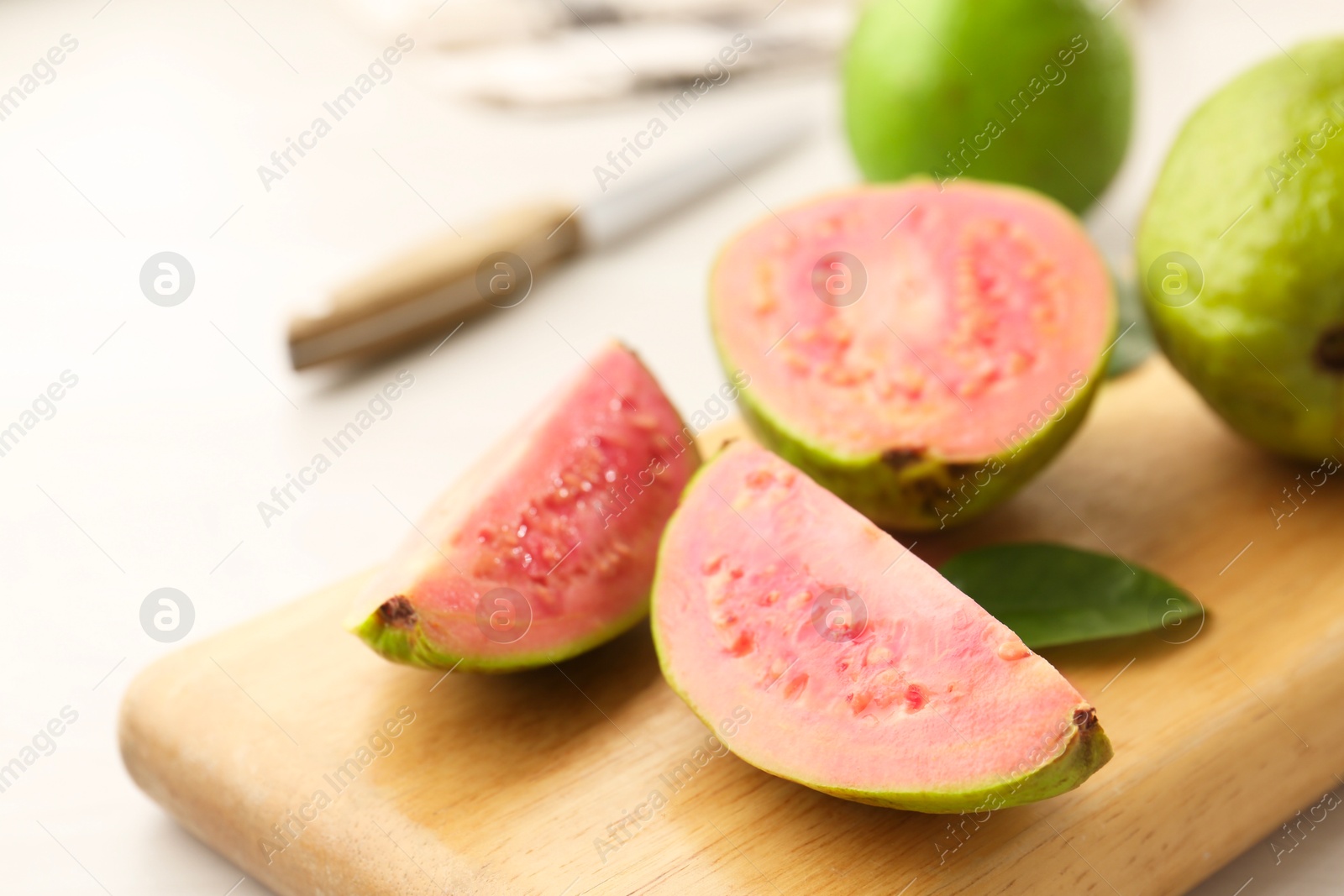 Photo of Fresh guava fruits and wooden board on white table, closeup