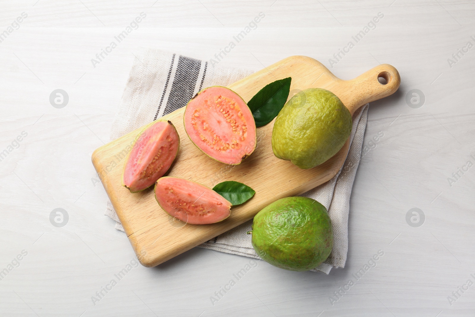 Photo of Fresh whole and cut guava fruits on white wooden table, top view