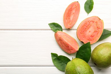 Photo of Fresh whole and cut guava fruits on white wooden table, flat lay. Space for text