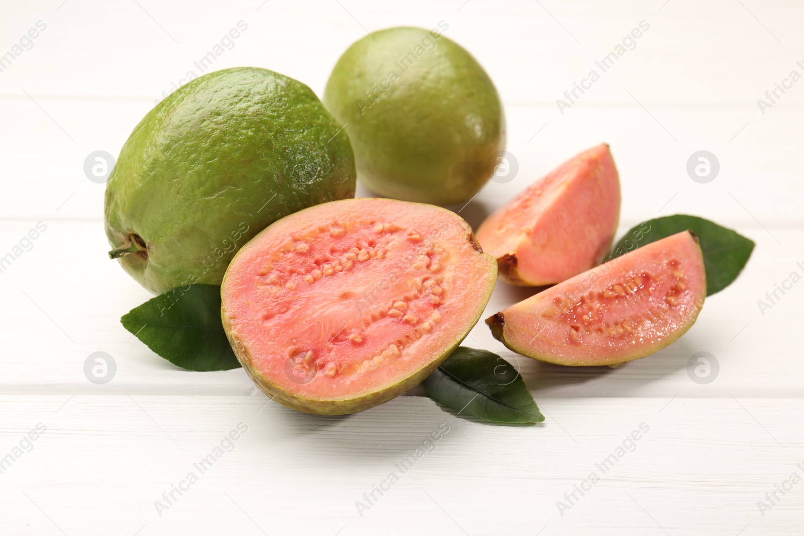 Photo of Fresh whole and cut guava fruits on white wooden table, closeup