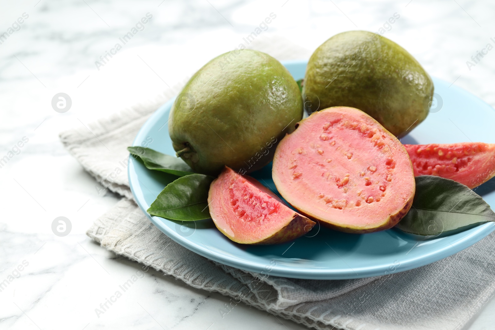 Photo of Fresh guava fruits and leaves on white marble table, closeup