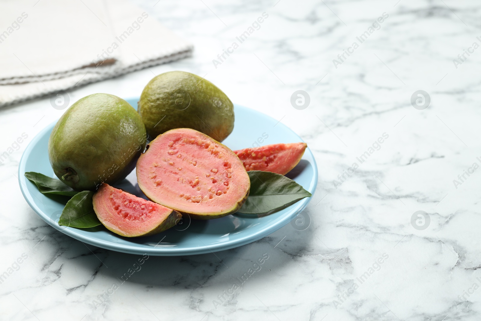 Photo of Fresh guava fruits and leaves on white marble table. Space for text