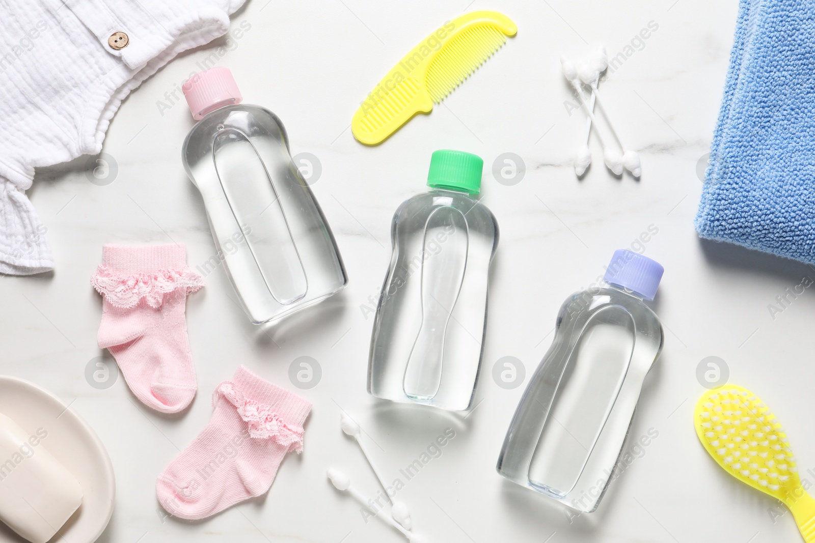 Photo of Baby oil, clothes and bath accessories on white marble background, flat lay