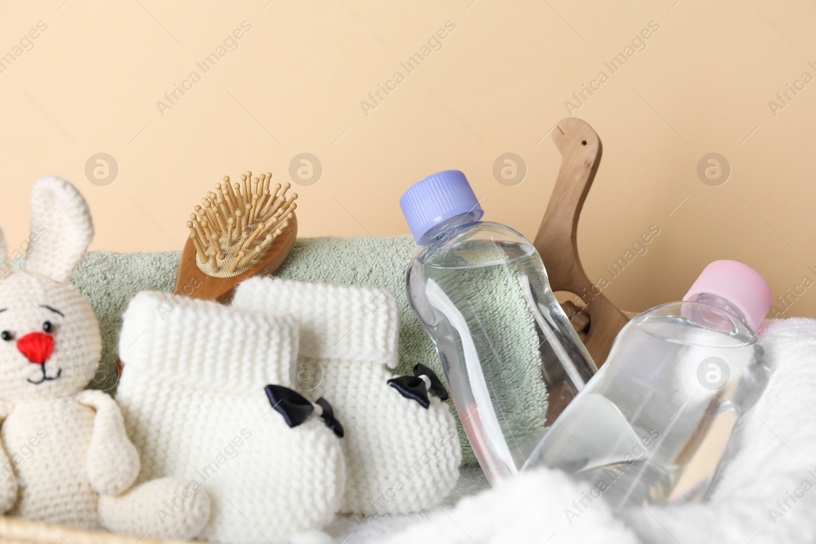 Photo of Baby oil and bath accessories in basket on beige background, closeup