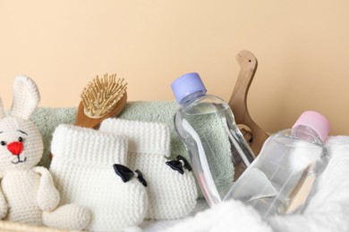 Photo of Baby oil and bath accessories in basket on beige background, closeup