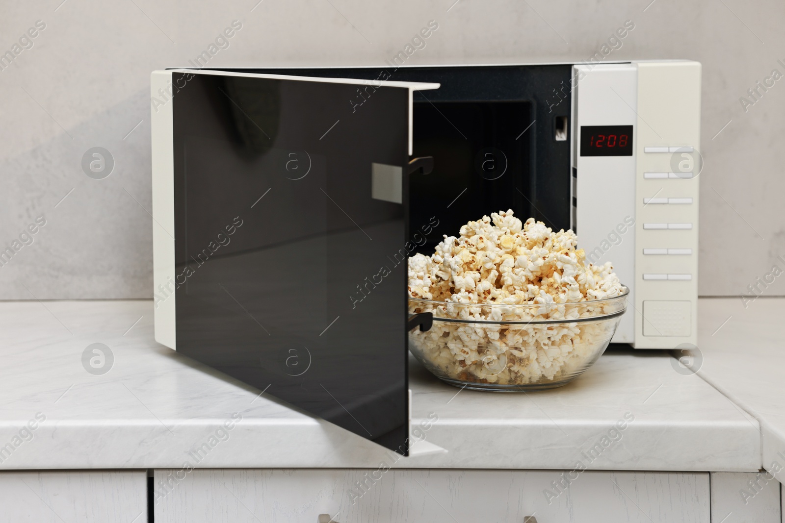 Photo of Tasty popcorn in bowl near microwave oven on white marble countertop indoors