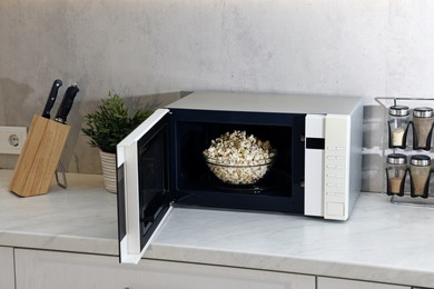 Photo of Open microwave oven with bowl of popcorn on white marble countertop in kitchen