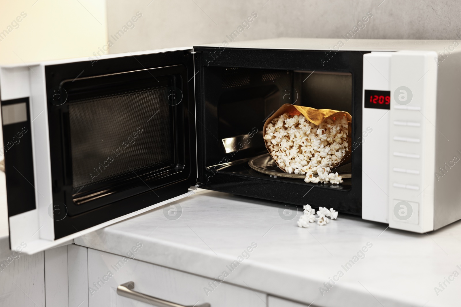 Photo of Open microwave oven with bag of popcorn on white marble countertop in kitchen