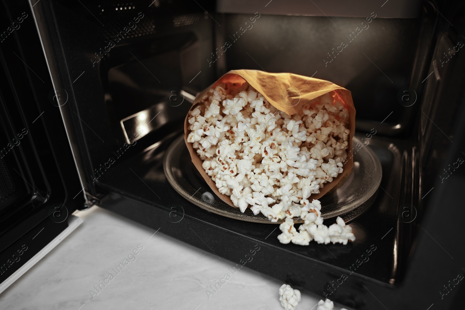 Photo of Open microwave oven with bag of popcorn on white marble table, closeup