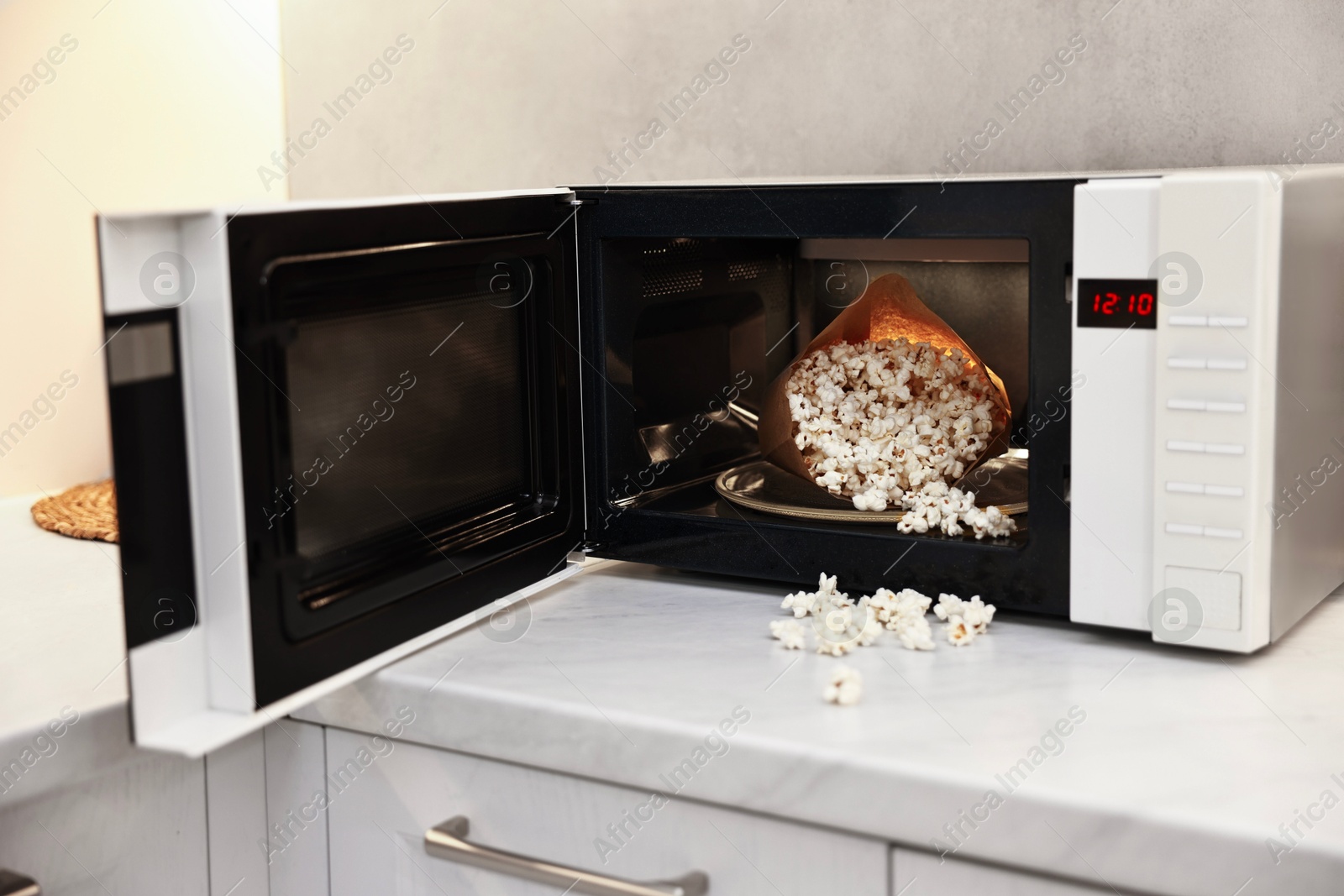 Photo of Open microwave oven with bag of popcorn on white marble countertop in kitchen