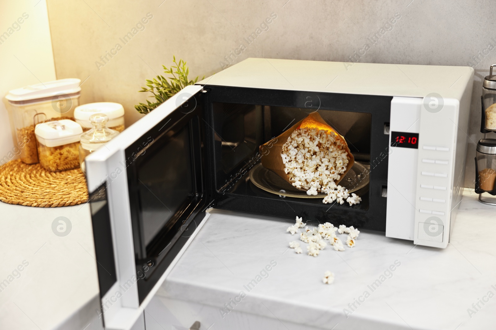 Photo of Open microwave oven with bag of popcorn on white marble countertop in kitchen