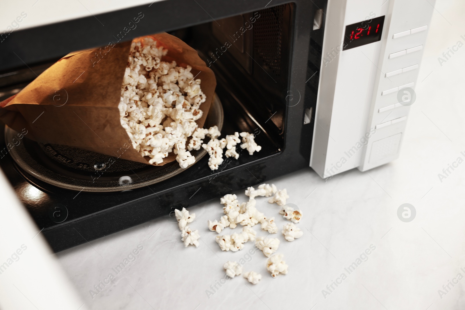 Photo of Open microwave oven with bag of popcorn on white marble table