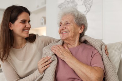 Photo of Granddaughter covering her grandmother with blanket at home. Elderly care