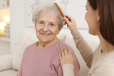 Photo of Granddaughter brushing her grandmother with comb at home, selective focus. Elderly care