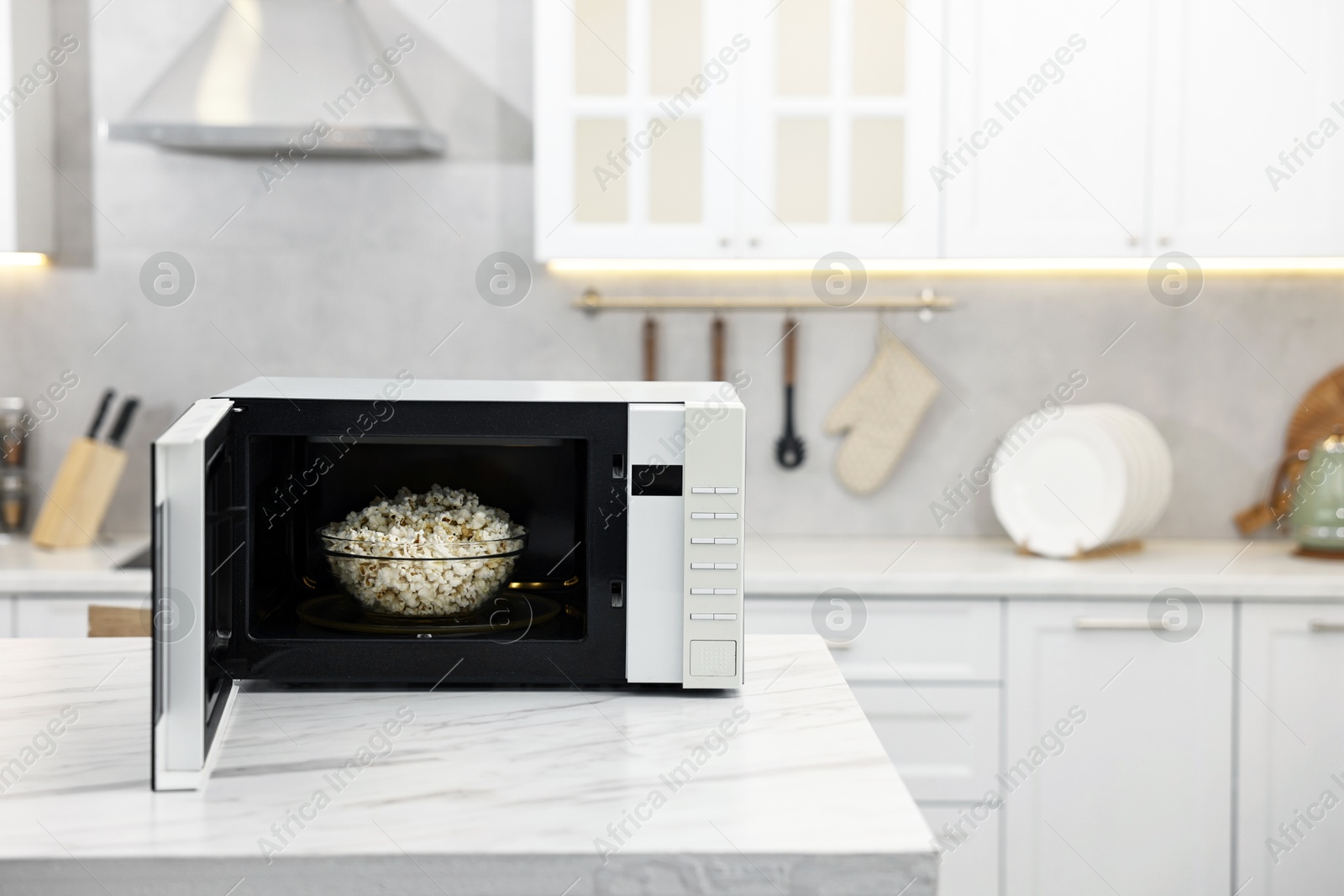 Photo of Open microwave oven with bowl of popcorn on white marble table in kitchen, space for text