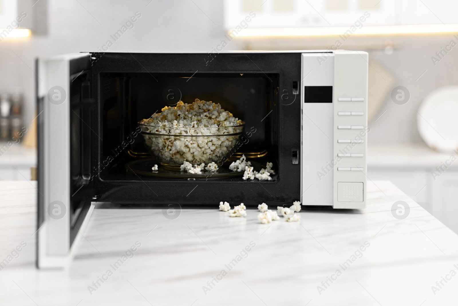 Photo of Open microwave oven with bowl of popcorn on white marble table in kitchen