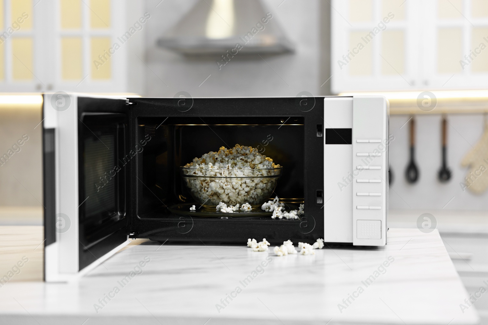 Photo of Open microwave oven with bowl of popcorn on white marble table in kitchen