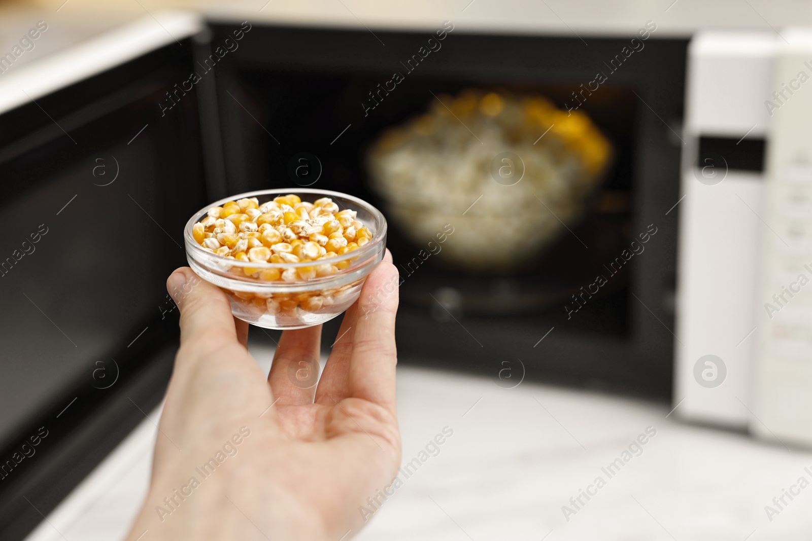 Photo of Woman with bowl of unpopped corn kernels near microwave oven indoors, closeup. Space for text