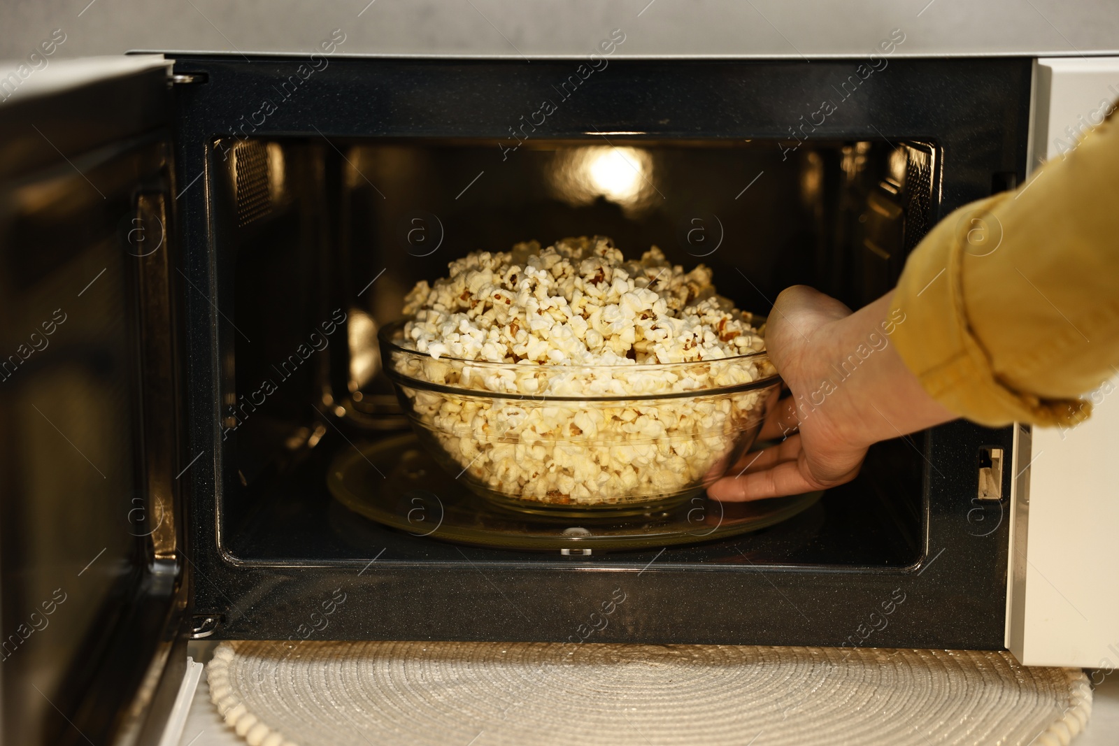 Photo of Woman taking bowl with popcorn out of microwave oven, closeup