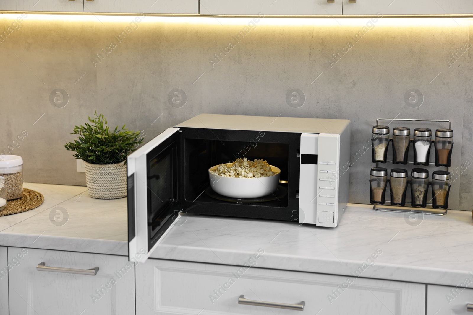 Photo of Open microwave oven with bowl of popcorn on white marble countertop in kitchen