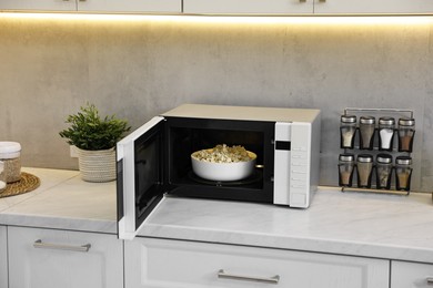 Photo of Open microwave oven with bowl of popcorn on white marble countertop in kitchen