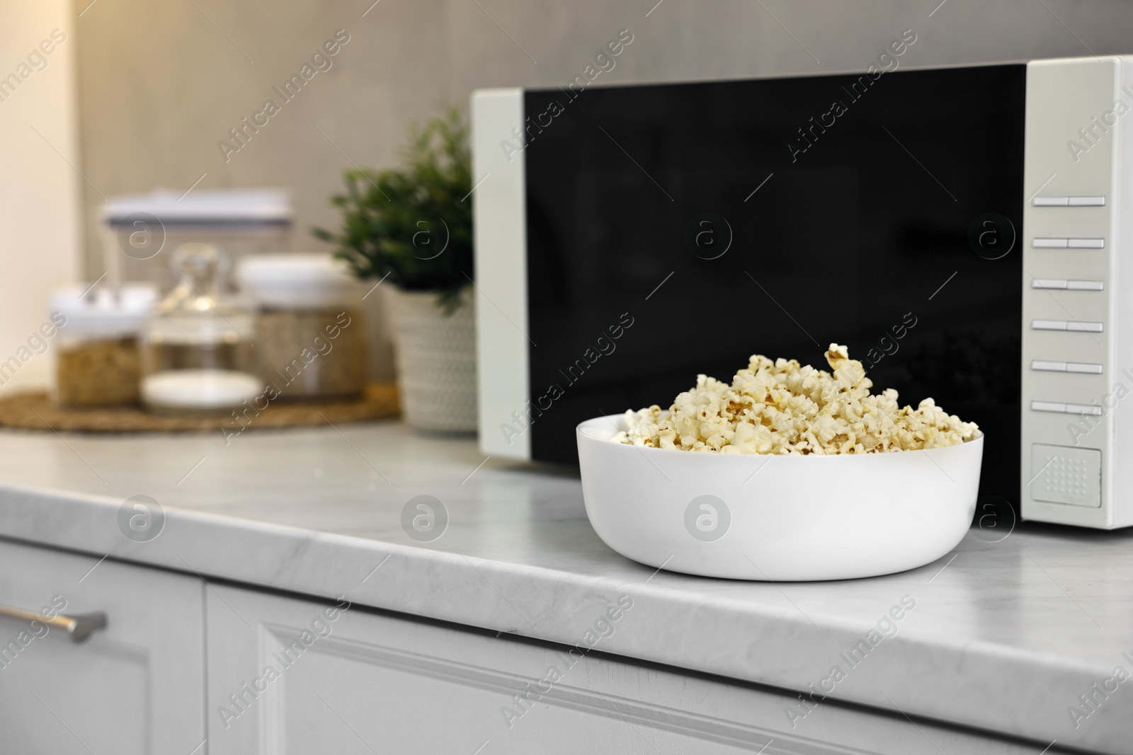 Photo of Bowl of popcorn near microwave oven on white marble countertop in kitchen