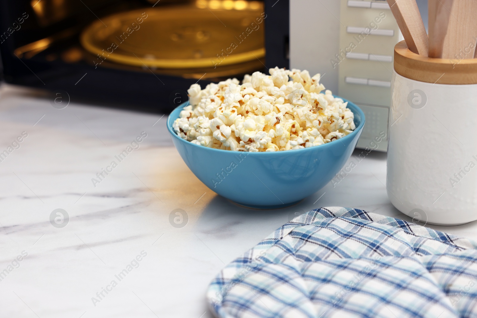 Photo of Tasty popcorn in bowl near microwave oven on white marble table