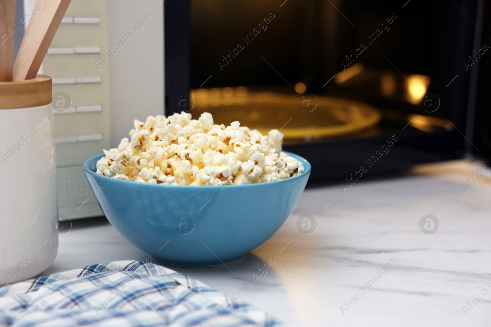 Photo of Tasty popcorn in bowl near microwave oven on white marble table, space for text