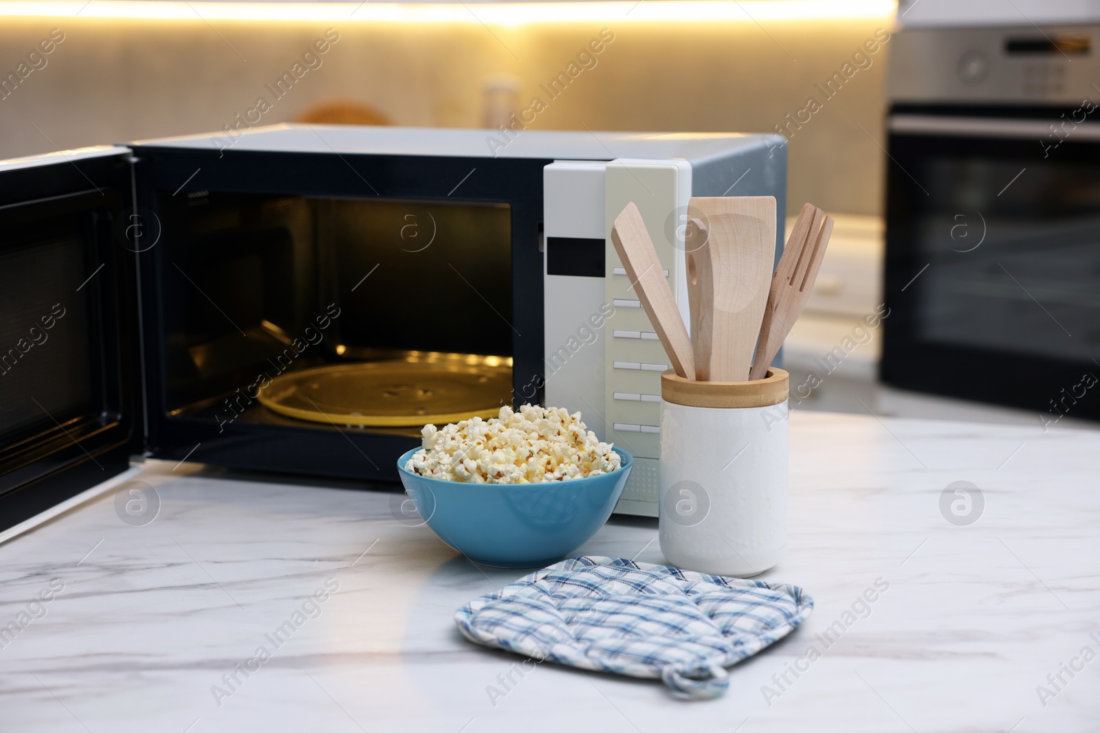 Photo of Tasty popcorn in bowl near microwave oven on white marble table indoors