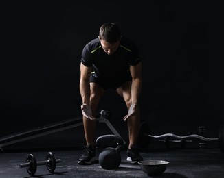 Photo of Man with talcum powder on hands training with kettlebell against black background