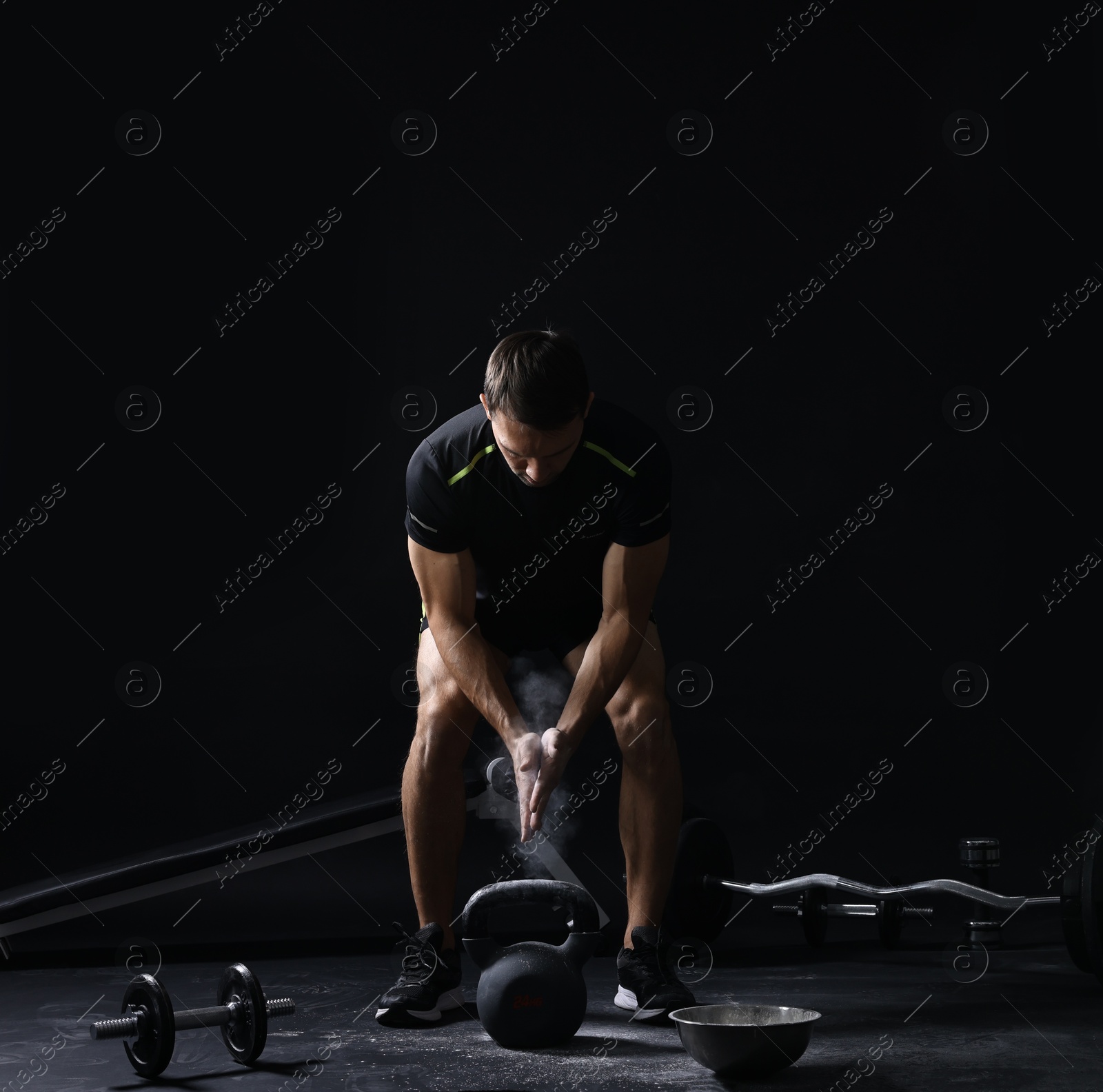 Photo of Man clapping hands with talcum powder before training with kettlebell on black background