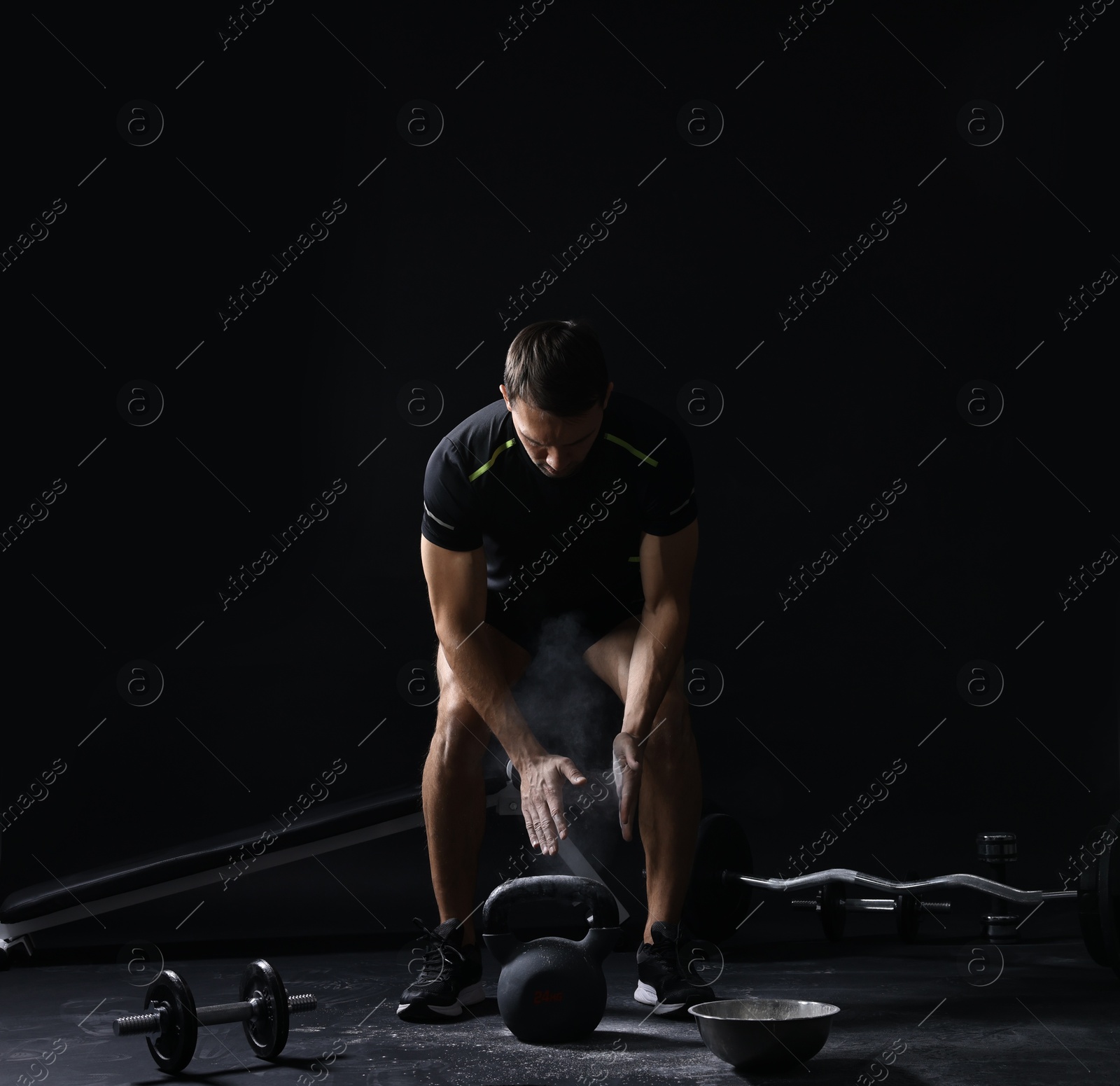 Photo of Man clapping hands with talcum powder before training with kettlebell on black background