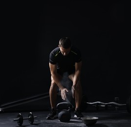 Photo of Man clapping hands with talcum powder before training with kettlebell on black background