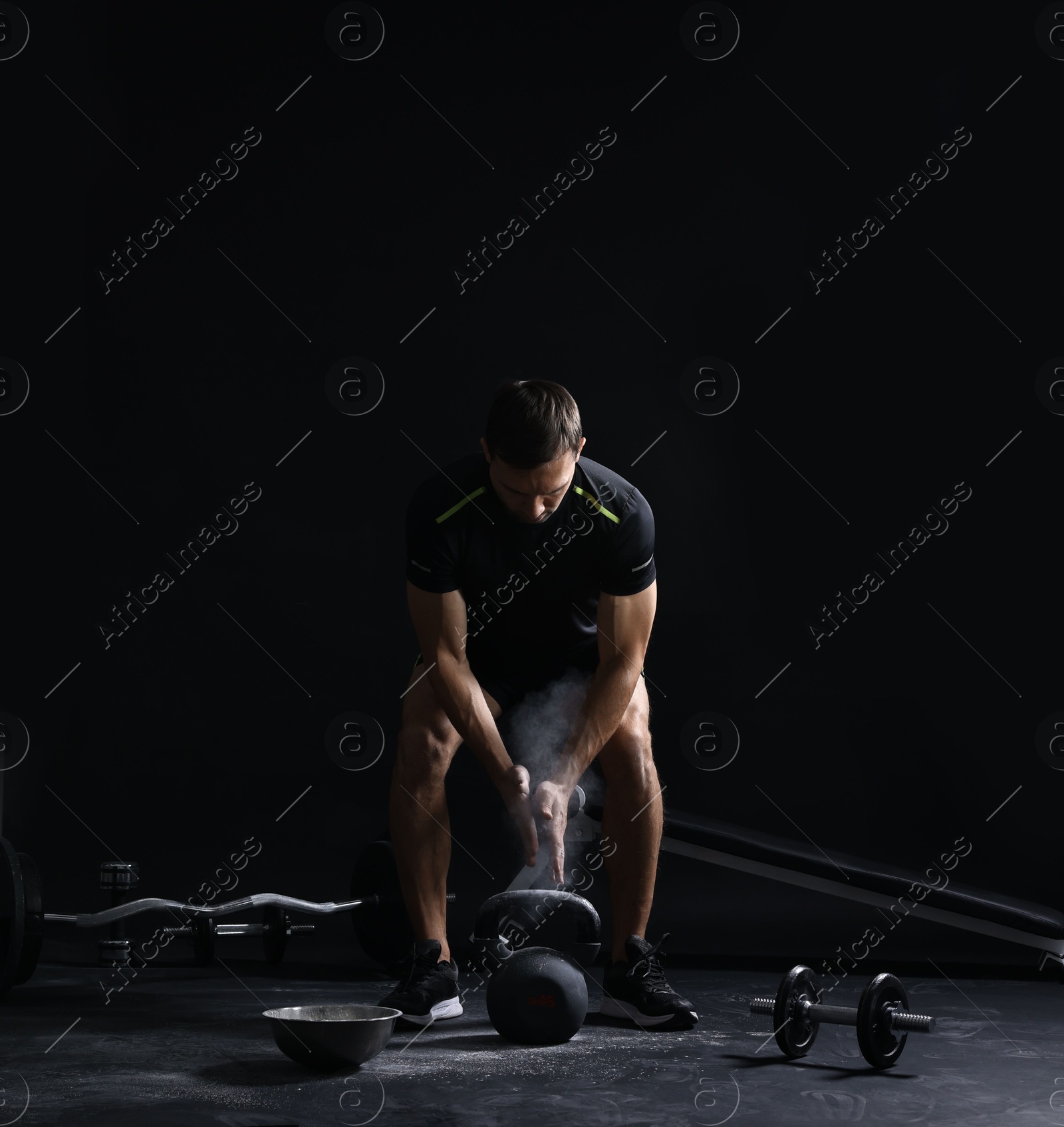 Photo of Man clapping hands with talcum powder before training with kettlebell on black background