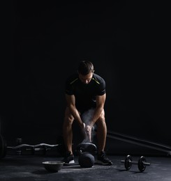 Photo of Man clapping hands with talcum powder before training with kettlebell on black background